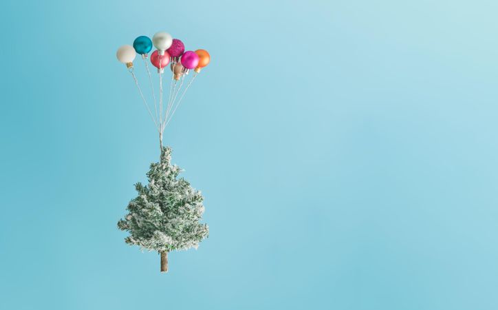 Christmas tree lifted up by colorful balloon