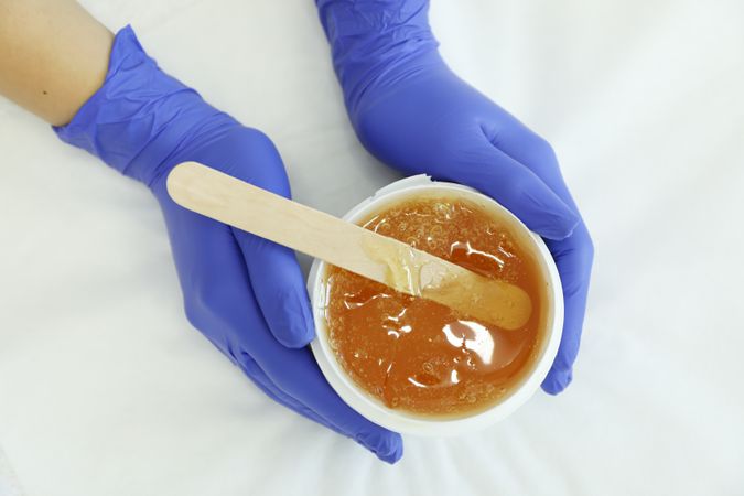 Female hands holding liquid yellow paste for sugaring on plain background, top view