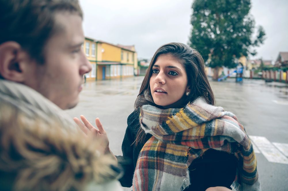 Woman having argument with man outside on rainy autumn day