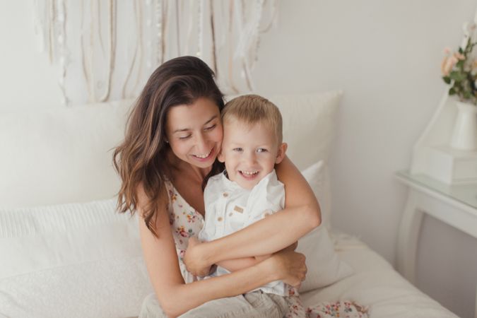 Mother ticking little son and laughing on bed