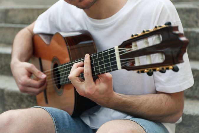 Young man sits on the steps and play on guitar