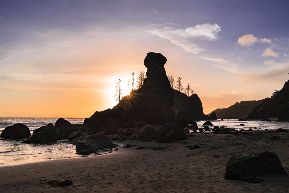 Beautiful tranquil beach with sun coming behind the rocks