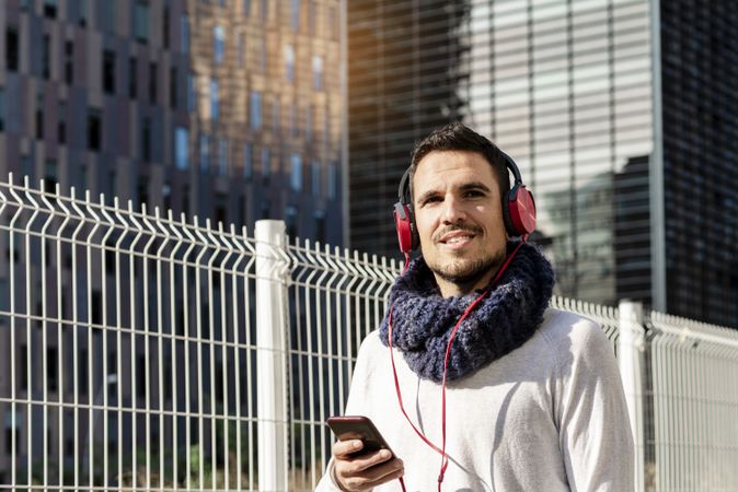 Content man listening to music on headphones while holding a mobile phone outdoor