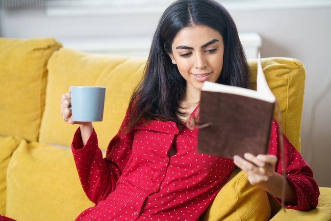 Woman relaxing in red pajamas reading at home with book
