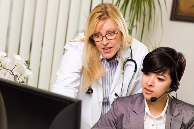 Female Doctor Discusses Work on Computer with Receptionist Assistant
