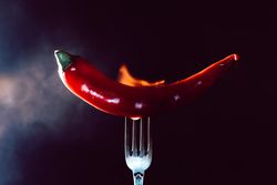 red chili pepper on fire in fork on a dark background