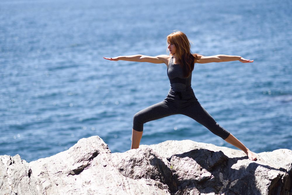 Young woman doing warrior pose on rocks at the beach
