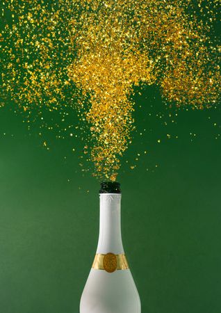 Champagne bottle explosion with golden glitter on green background