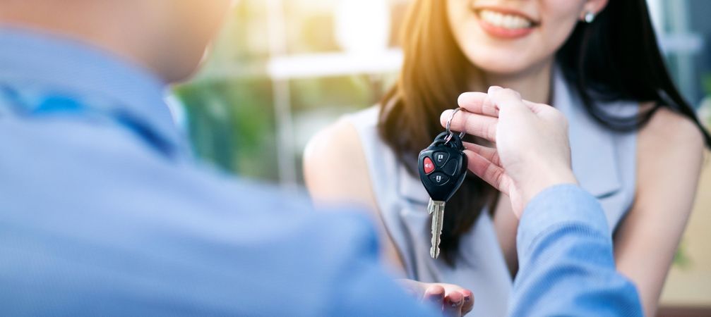 Happy Asian woman receiving remote from dealer sales man for buy new car