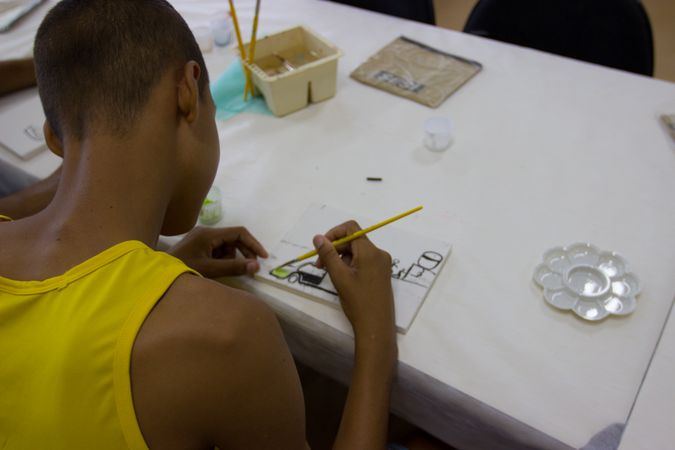 Teenage boy in yellow tank top painting with water color