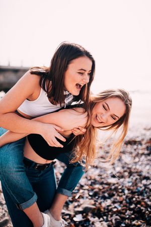 Two young woman having fun with one giving the other a piggyback on the beach