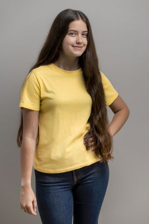 Portrait of young woman wearing a blank yellow t-shirt for mockup, casual style on grey background.
