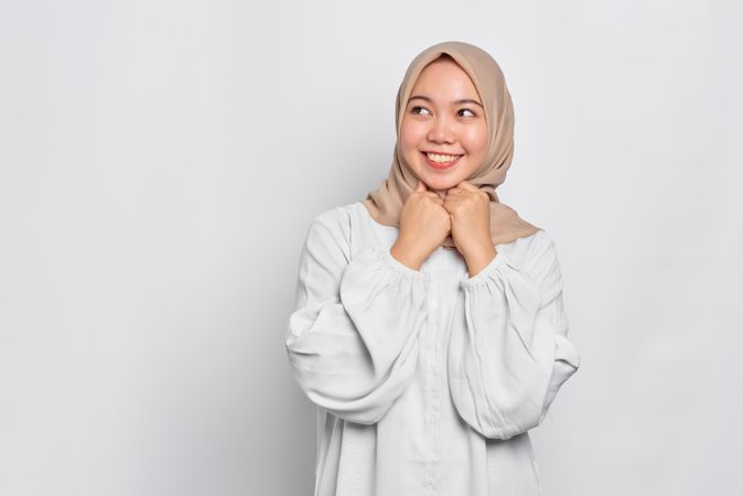 Happy Muslim woman in headscarf in light blouse with hands under her chin looking cute