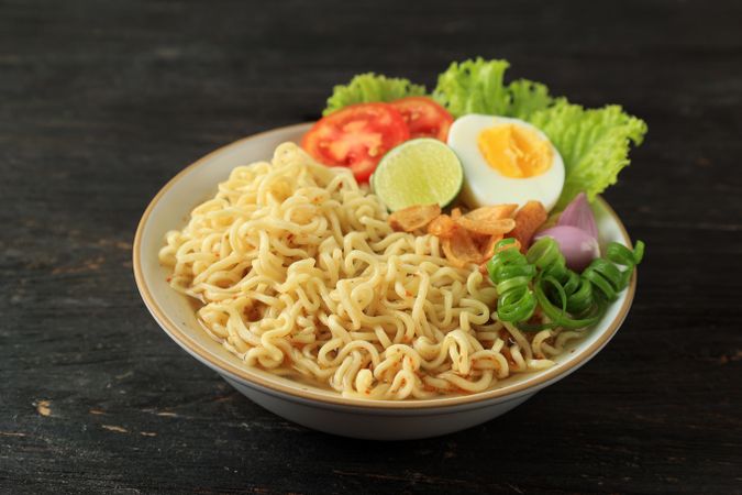 Indomie Rebus or Instant Boiled Noodle with Boiled Egg, Tomato, and Sliced Lime.