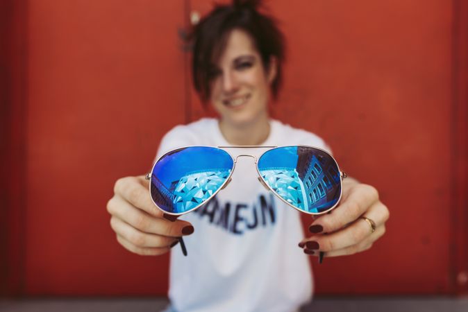 Young woman sitting on steps near door and showing sunglasses