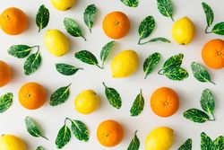 Pattern made of oranges, lemons and green leaves on bright background