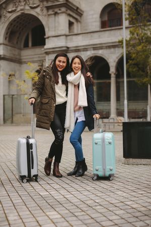 Two happy friends smiling and hugging with suitcases