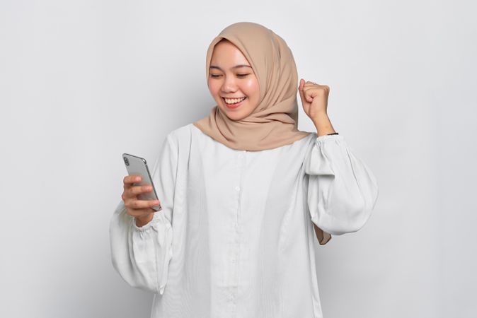 Asian female in headscarf receiving happy news on her cell phone