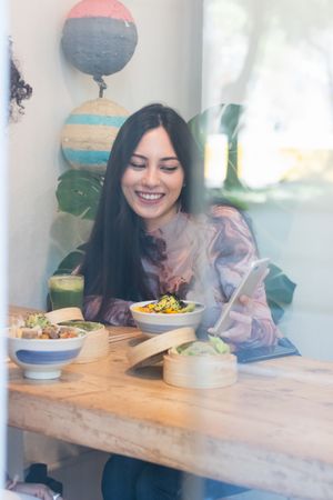 Smiling woman eating in restaurant while using mobile phone