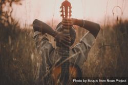 Man holding classical guitar while sitting on grass field during sunset 4dkBn5