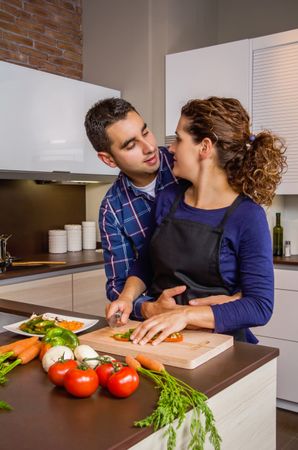 Loving couple in kitchen together as woman chops vegetables in kitchen