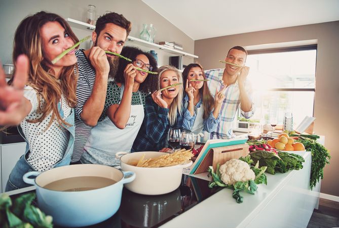 Multi-ethnic friends making silly faces with asparagus while cooking dinner
