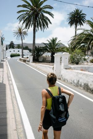 Back of sporty woman walking on quiet trees surrounded by palm trees
