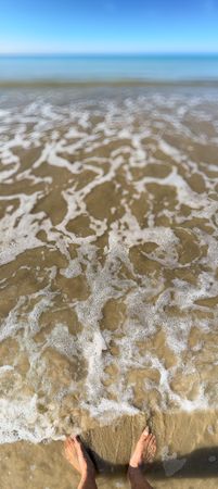 Parnoramic view of feet in the sand and foam at low tide, Ile de Ré, France