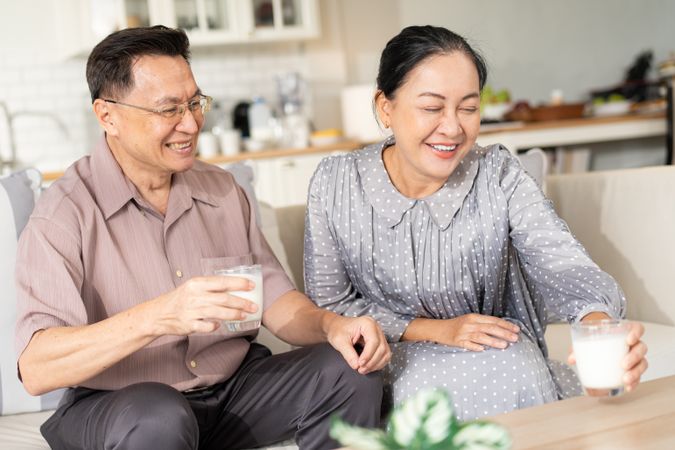 Happy Asian older couple holding glass of milk and drinking together