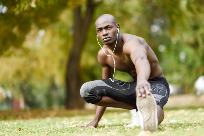 Healthy male stretching lower body with shirt off listening to music on headphones