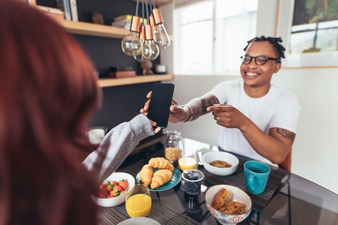 Man showing his mobile phone to his girlfriend sitting at breakfast table