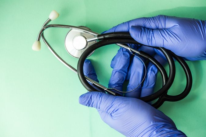 Looking down at green table with hands in blue latex gloves holding stethoscope