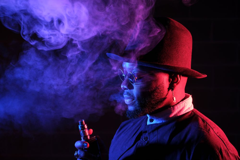 Stylish Black man smoking e cigarette in dark room