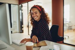 Woman with curly hair smiling at work working at a computer