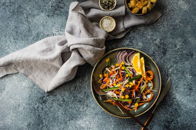 Top view of fresh salads with finely chopped vegetables and lemon slices in bowl on counter with copy space