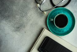 Looking down at coffee cup on teal plate, phone, stethoscope and notepad