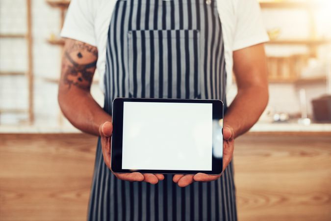 Close up shot of a man wearing an apron showing a digital tablet