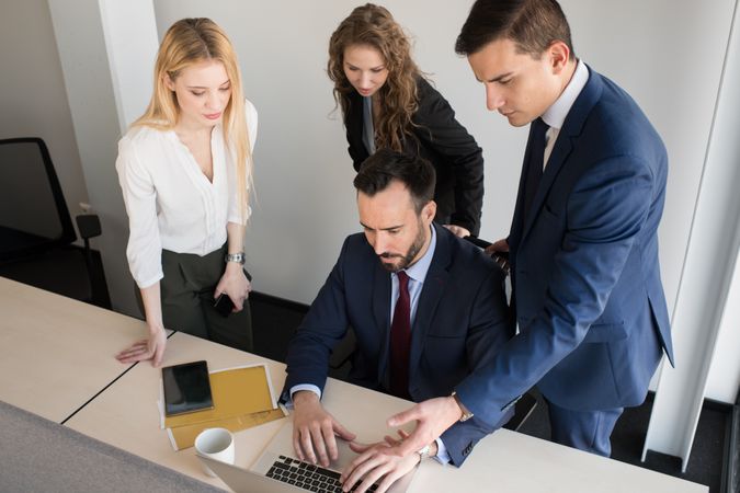 Stylish coworkers gathering around laptop in office