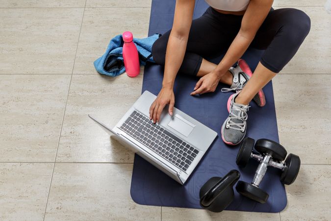 Cropped image of woman sitting on workout mat beside a computer