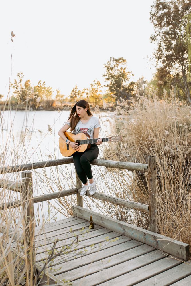 Young woman playing guitar near water