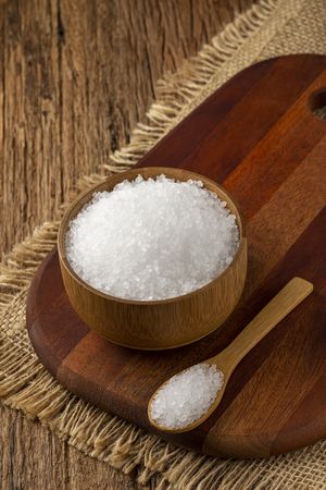 Coarse salt in bowl on wooden background.