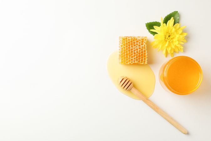Honeycomb, dipper, jar with honey and flower on neutral background, top view