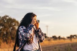 Young woman taking photos with analog camera in the field at sunset