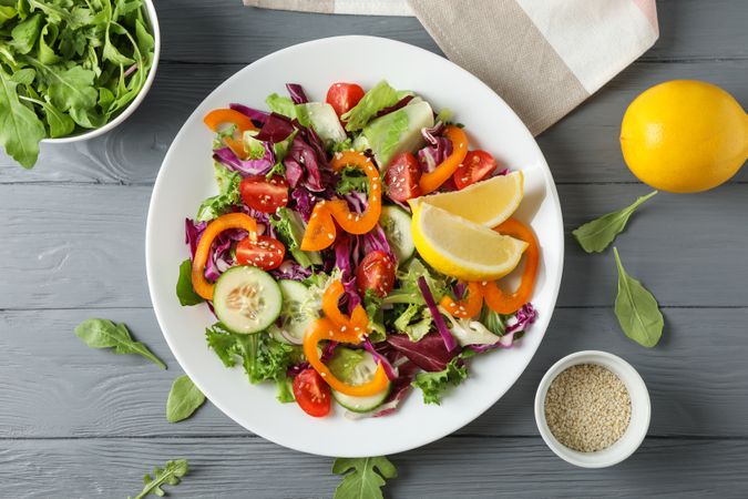 Plate with salad and ingredients on wooden background, top view