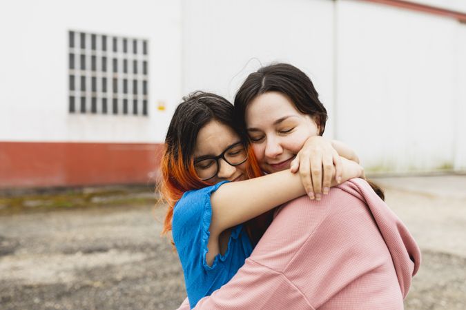 Two young women hug each other outside with eyes closed