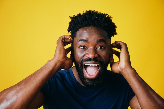 Portrait of joking Black man with both hands to his head on yellow background