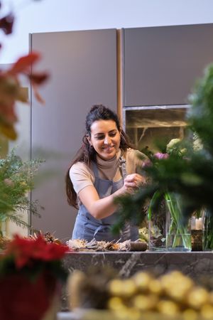Happy woman putting flowers in vase in floral shop