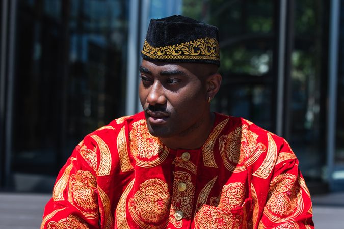 Thoughtful Black man in traditional clothes and headdress near building
