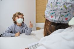 Boy showing approval gesture to doctor at table