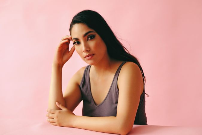 Pensive Hispanic woman looking at camera and sitting in pink room